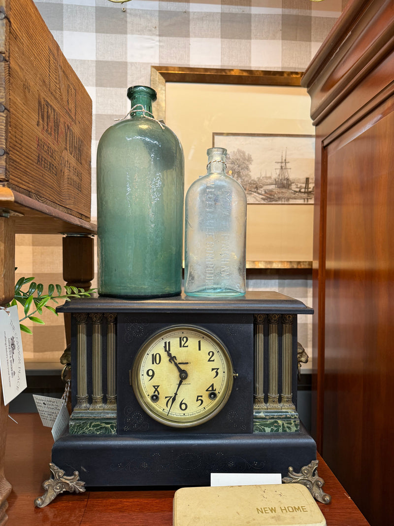 A historical mantel clock styled with vintage glass apothecary bottles, representing the antique collection at The Common Place