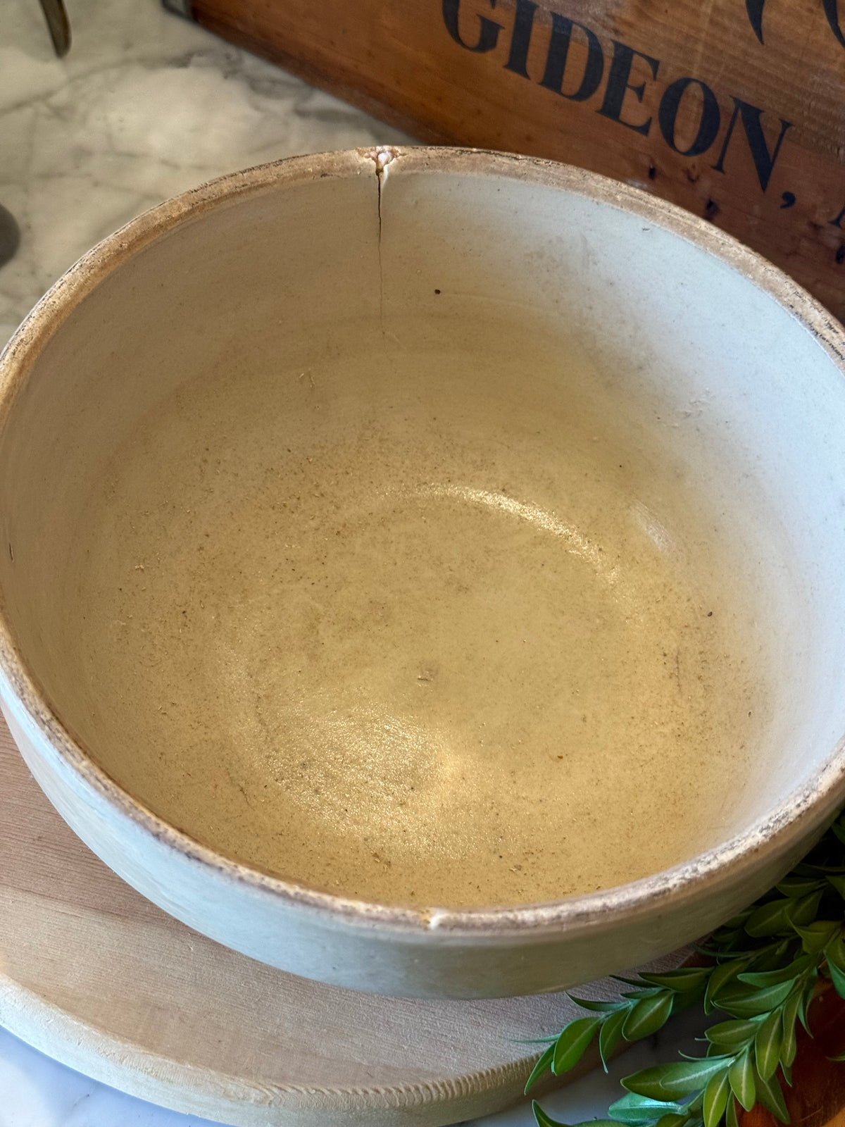 A handmade ceramic bowl with a rustic, hand-thrown finish, shown from a top-down perspective on a wooden board with marble and a wooden crate in the background.