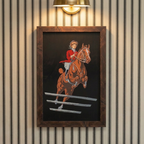 Archival 1909 equestrian print of jumping horse framed in warm walnut burl wood, hanging in a cozy traditional study with a collegiate, quiet luxury aesthetic.