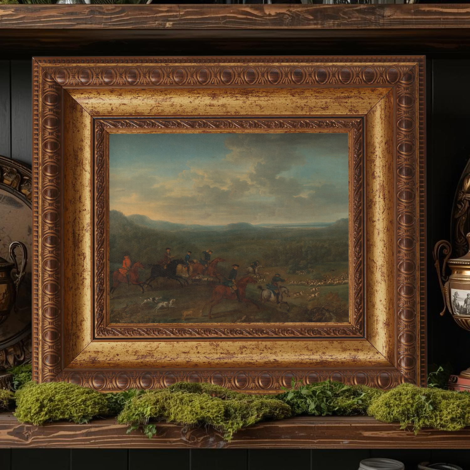 Decorative english hunting art in an ornate gold frame on a wooden shelf with greenery.