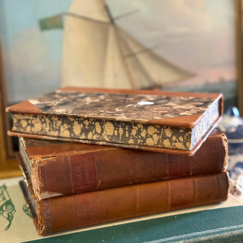 Stack of vintage marbled books with a sailboat painting in the background