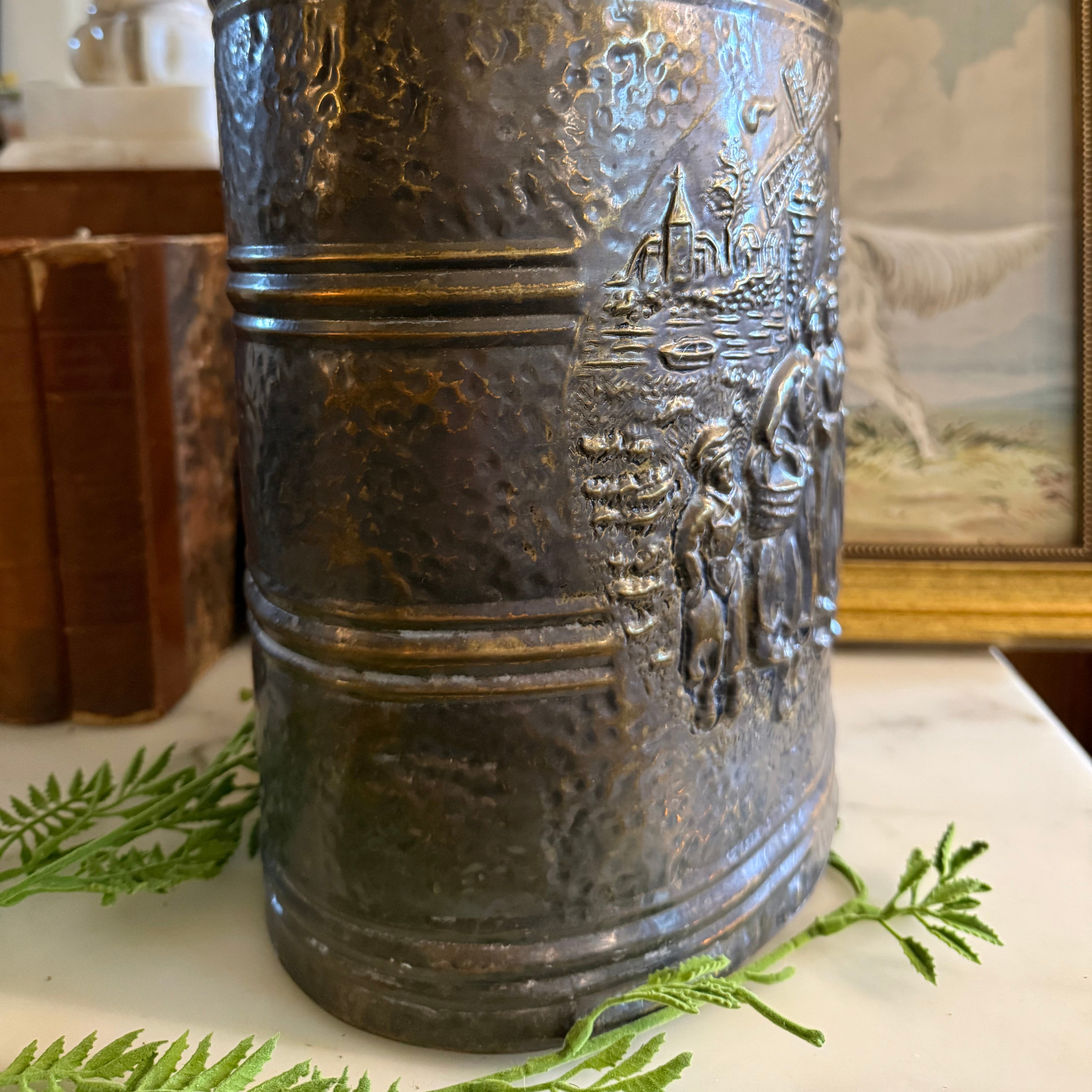 Close-up detail of the embossed figures and village relief on the brass umbrella stand.