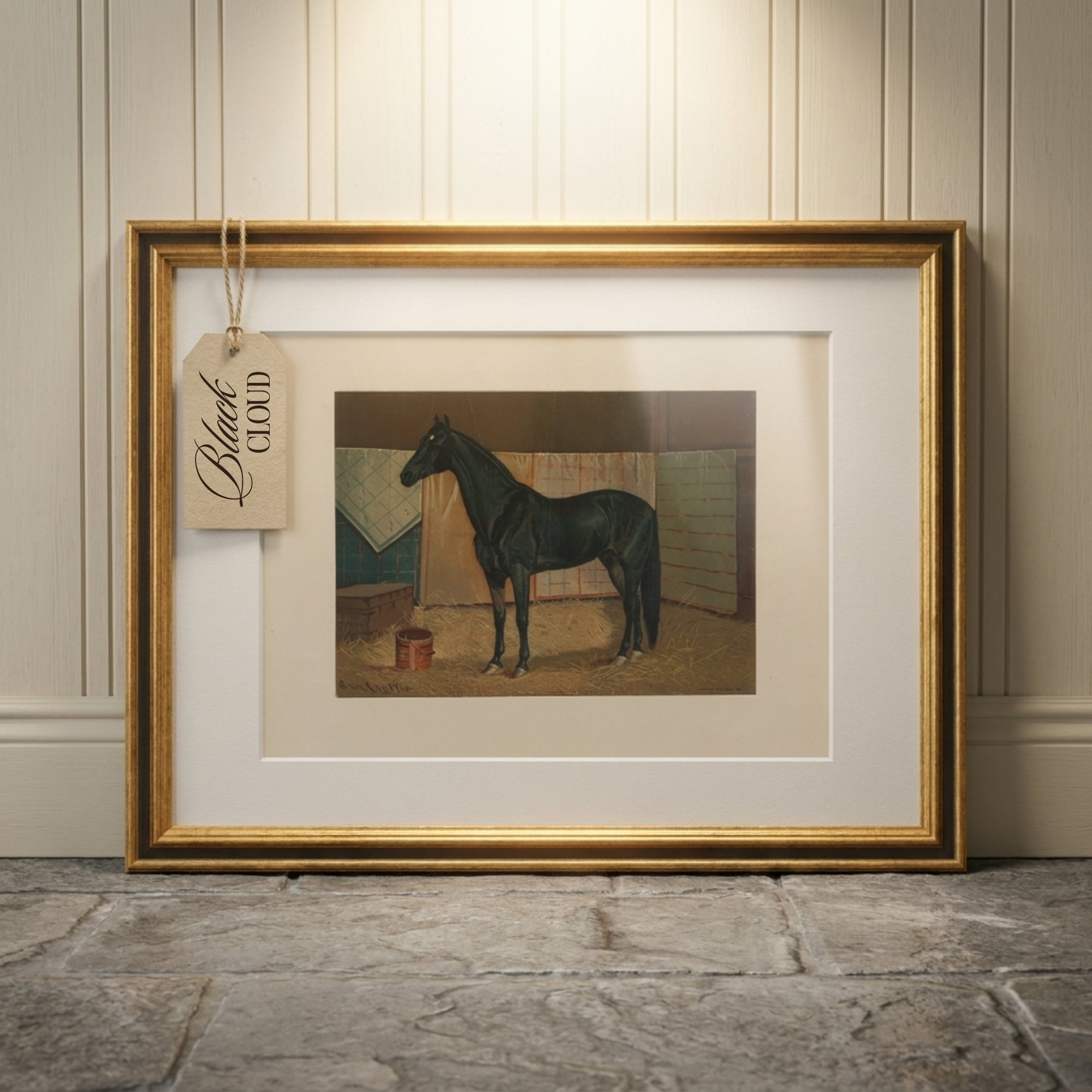 A framed art print featuring a black horse standing in a stable, displayed against a beige paneled wall on a stone floor. The frame is gold with a wide white mat, and a hanging tag reads 'Black Cloud'.