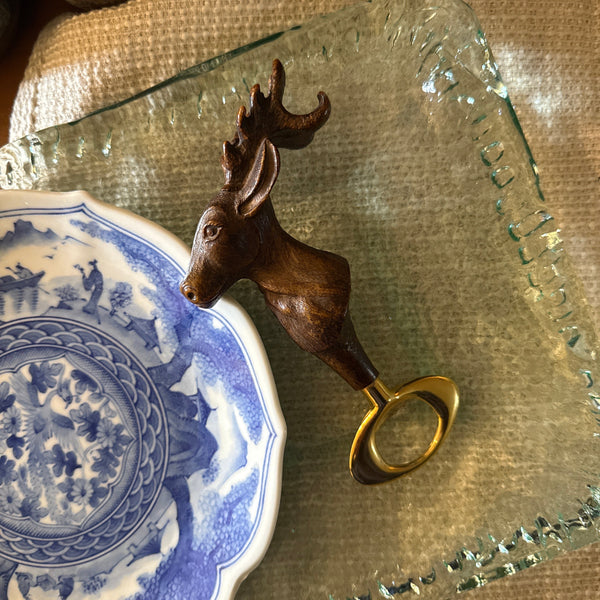 Decorative deer bottle opener shaped like a deer head on a blue and white ceramic plate.