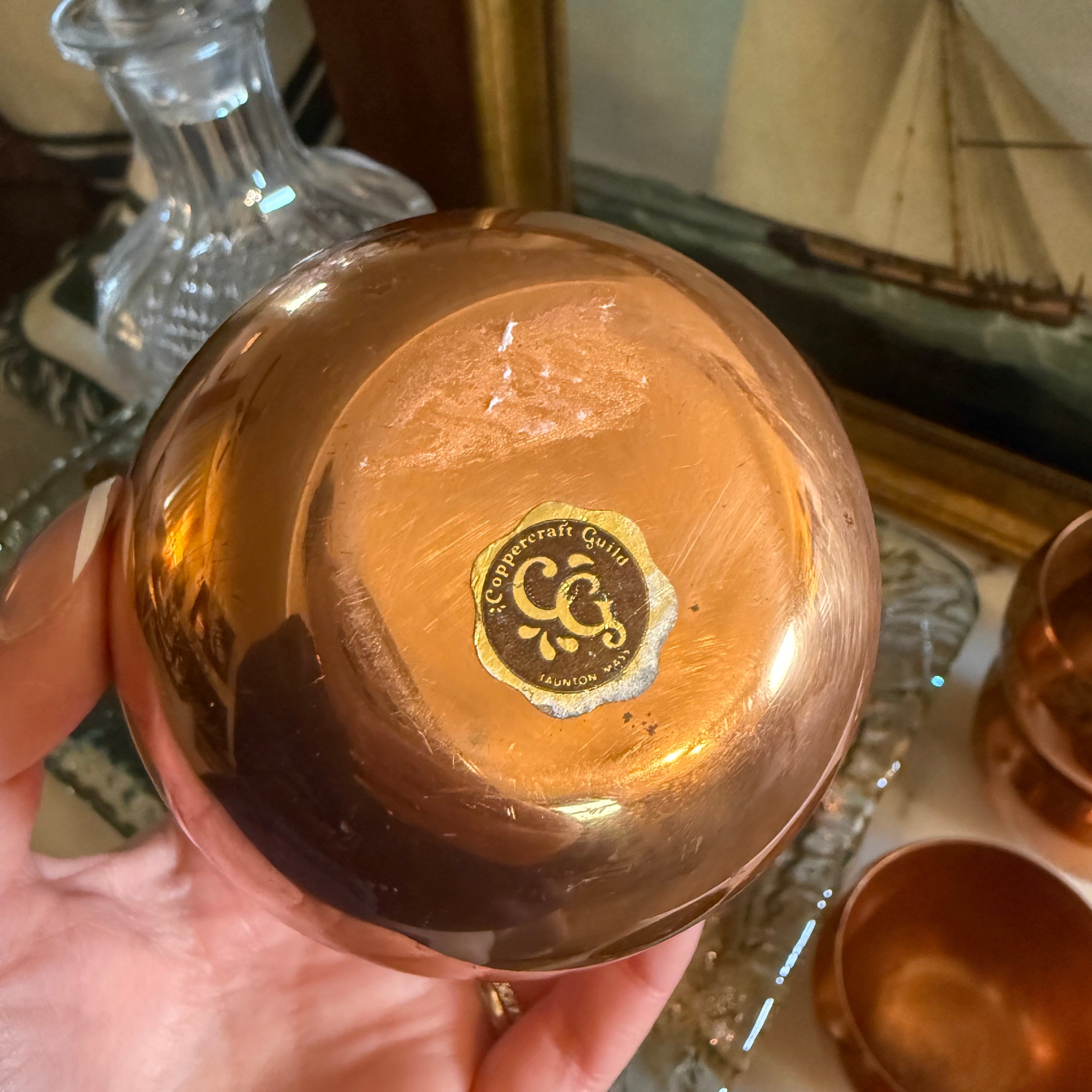 Hand holding a gold cups with a Coppercraft Guild brand logo, blurred background