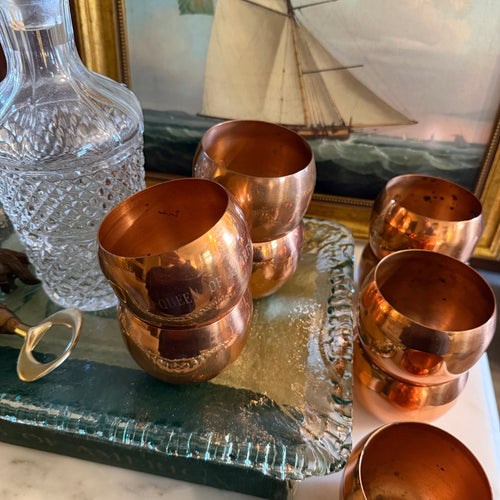 Set of 9 vintage Coppercraft Guild MCM copper tumbler drinking cups on a stack of books