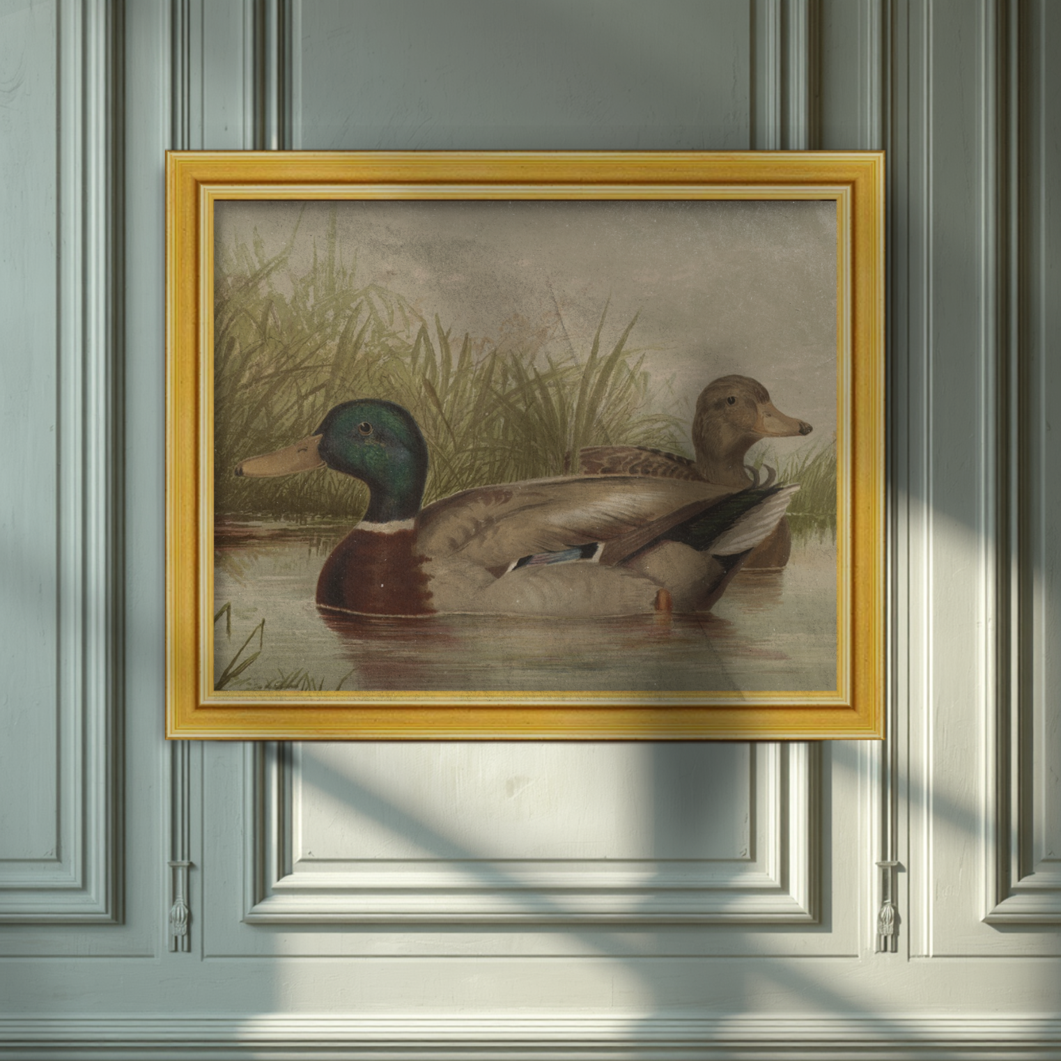 A framed vintage-style painting of two ducks in shallow water with reeds, hung on a paneled wall. The frame is gold-toned, and the wall behind is a muted blue-gray with soft diagonal shadows across it.