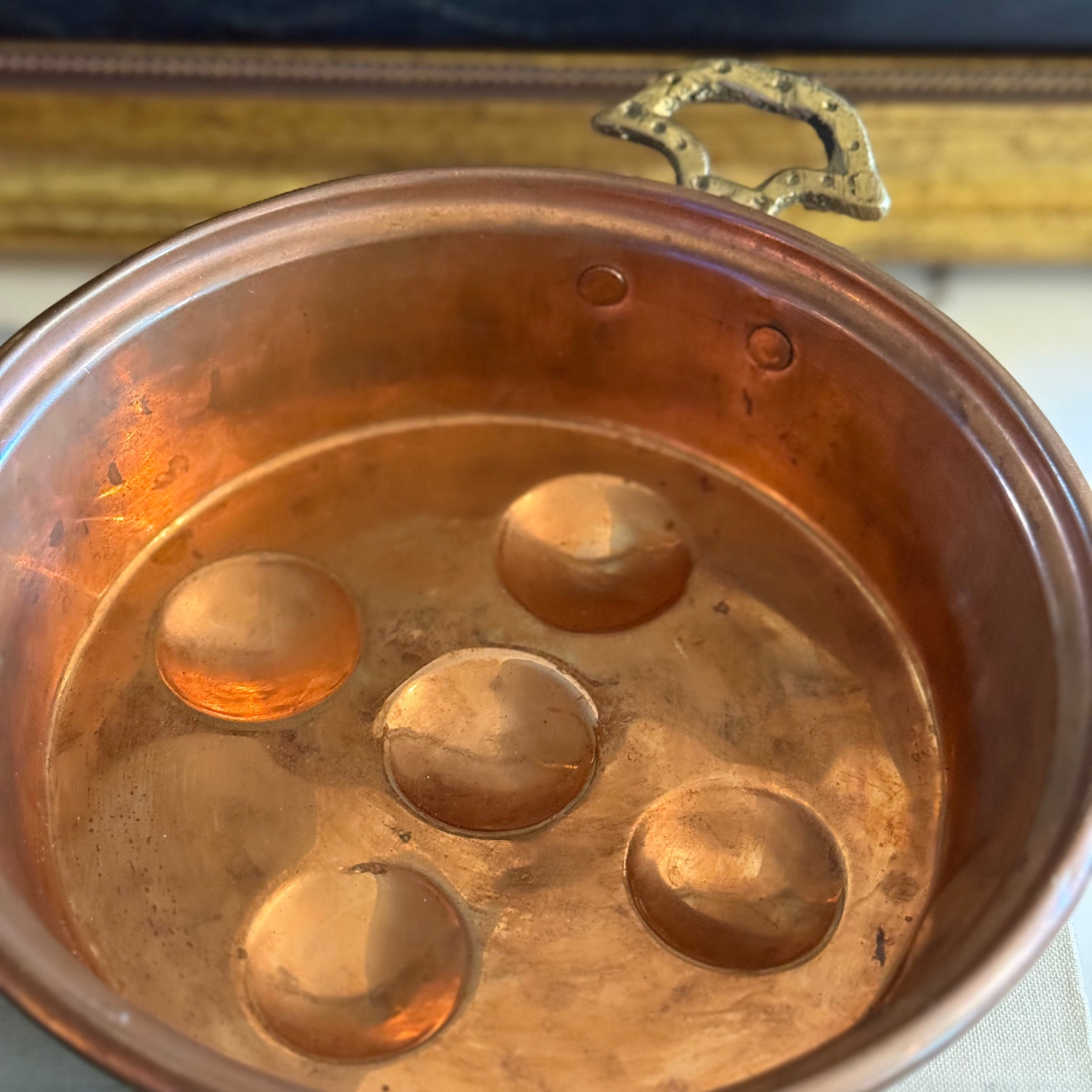 Side profile of a copper egg poacher against a nautical vintage painting backdrop.