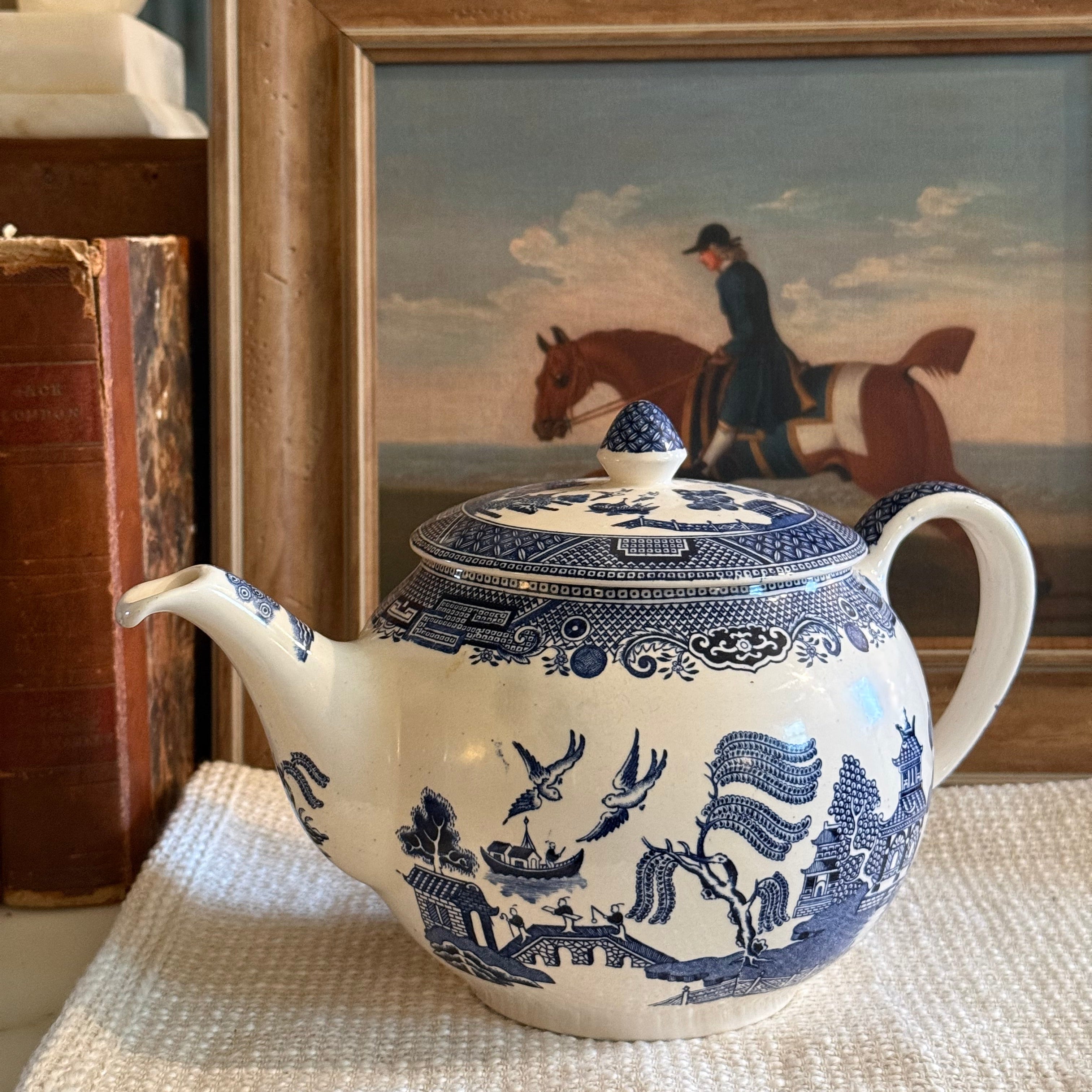 Classic Johnson Bros Blue Willow blue and white ironstone teapot on a white linen cloth with framed equestrian portrait in back