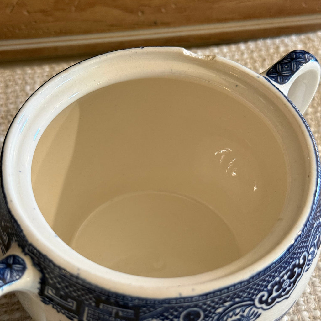 Close up of a small chip on the rim of a vintage blue and white sugar bowl.