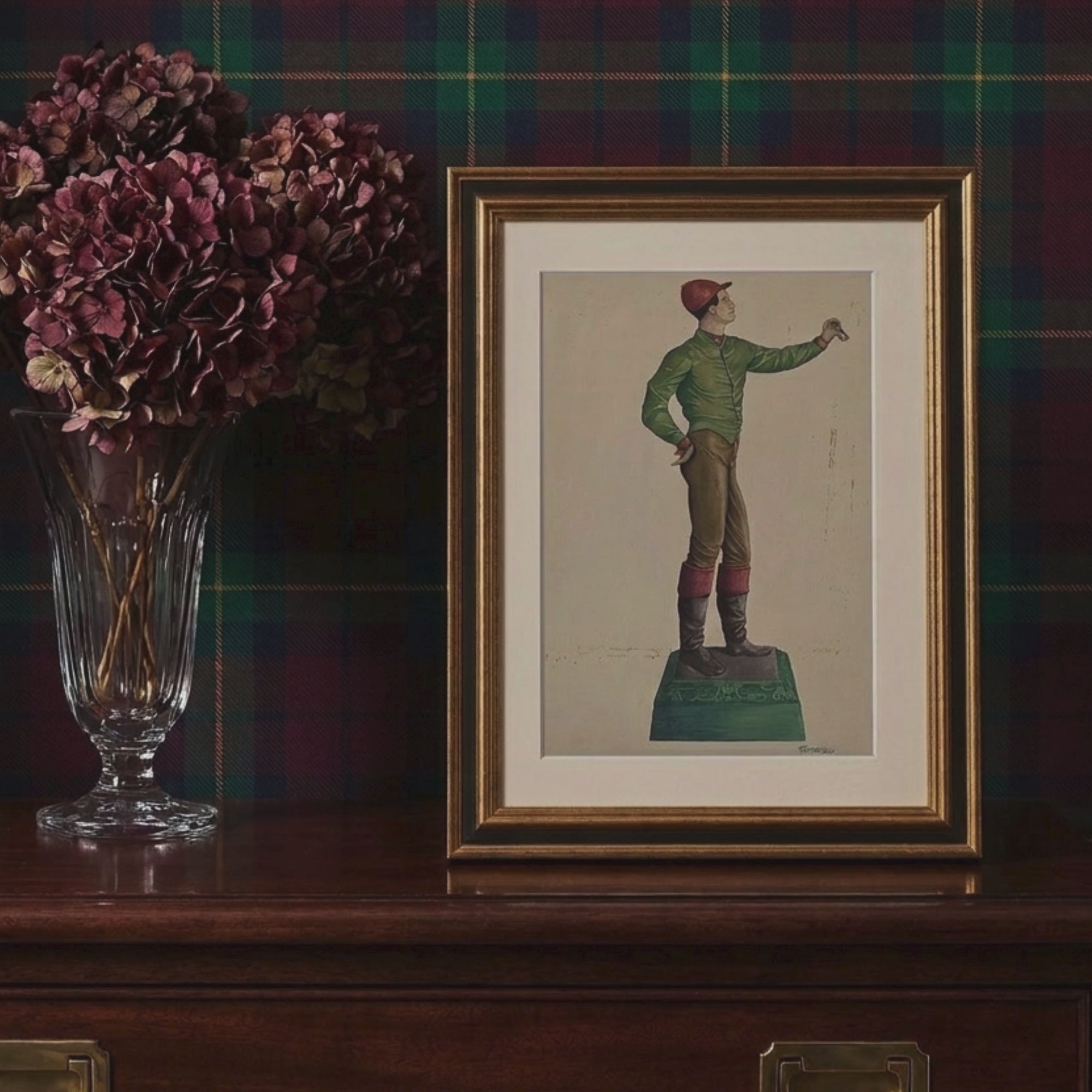 Video showcase of the framed 1938 Frank Gray jockey hitching post fine art print, displayed on a dark wood cabinet against a green tartan plaid wall beside dried burgundy flowers in a crystal vase.