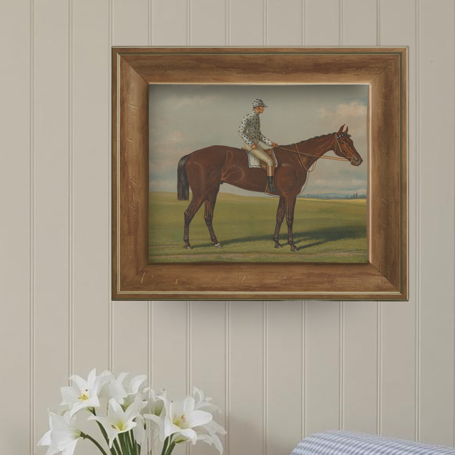 Framed painting of a jockey on a horse against a neutral wall with flowers in the foreground.