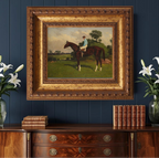 Framed painting of a horse and rider on a wooden dresser with decorative books and flowers against a blue wall.