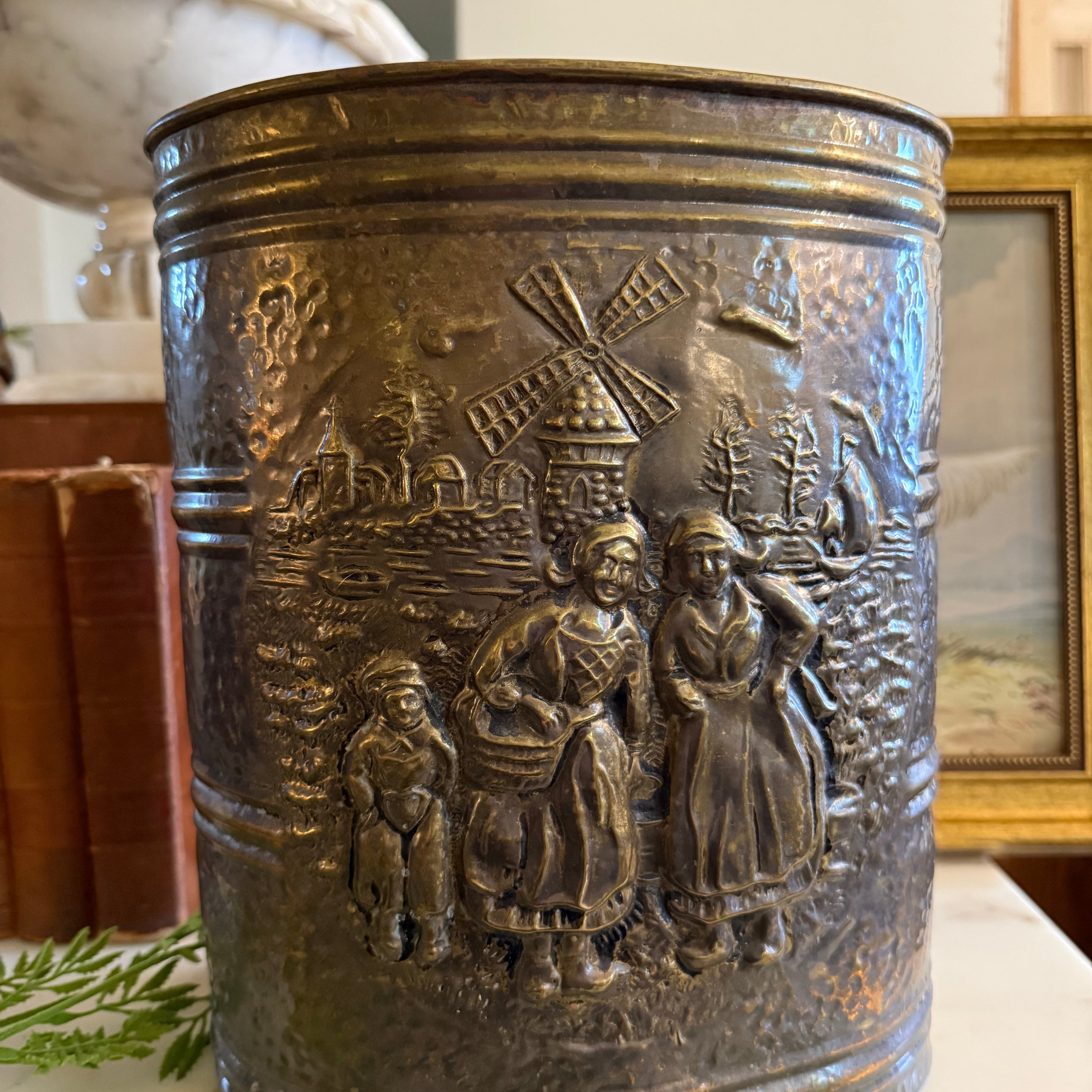 Front view of a vintage English brass umbrella holder with embossed Dutch windmill scene.