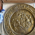 Vintage circular embossed brass wall plate featuring a detailed English pub scene with people at a table.