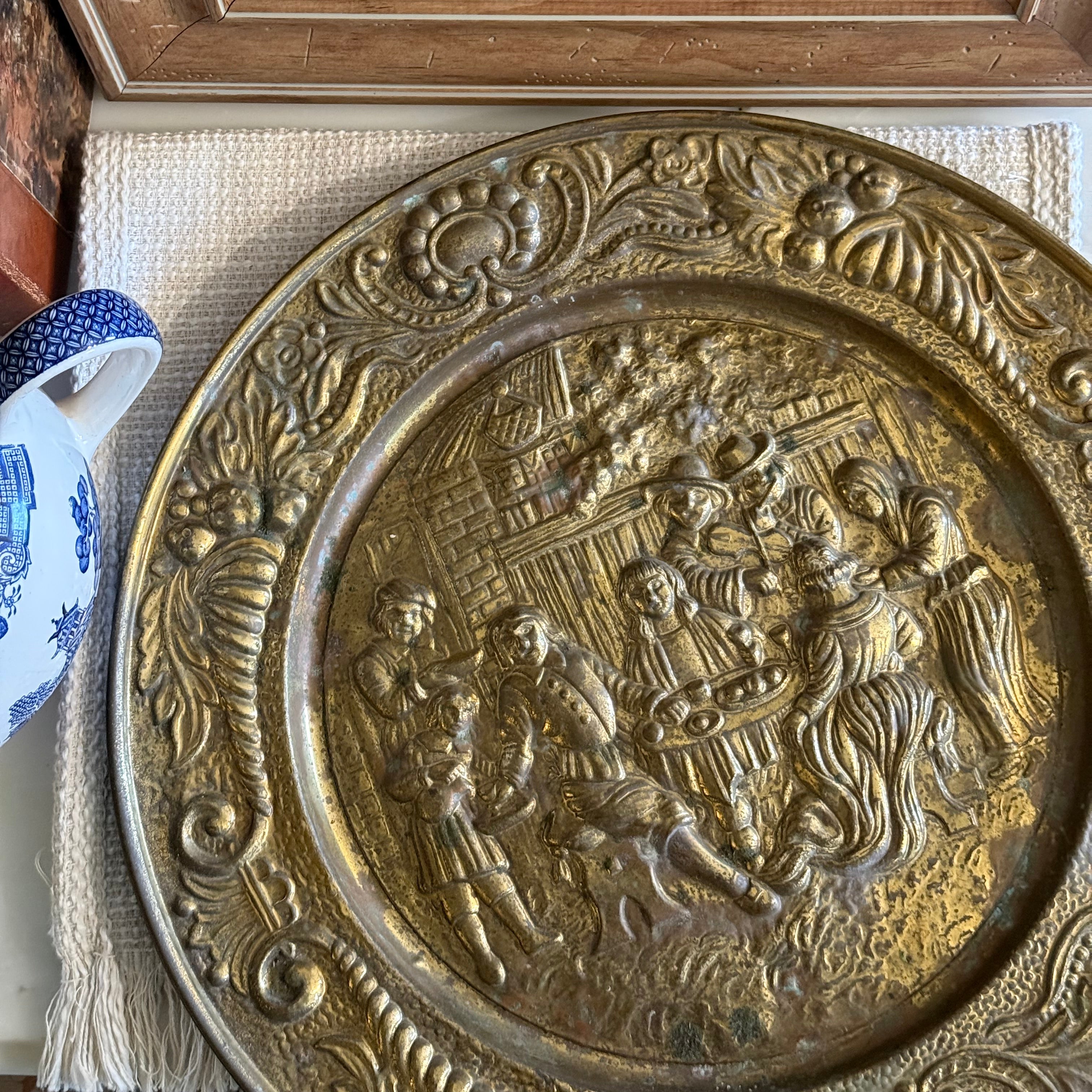 Vintage circular embossed brass wall plate featuring a detailed English pub scene with people at a table.