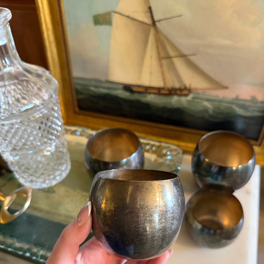 Hand holding a silver goblet in front of a sailboat painting