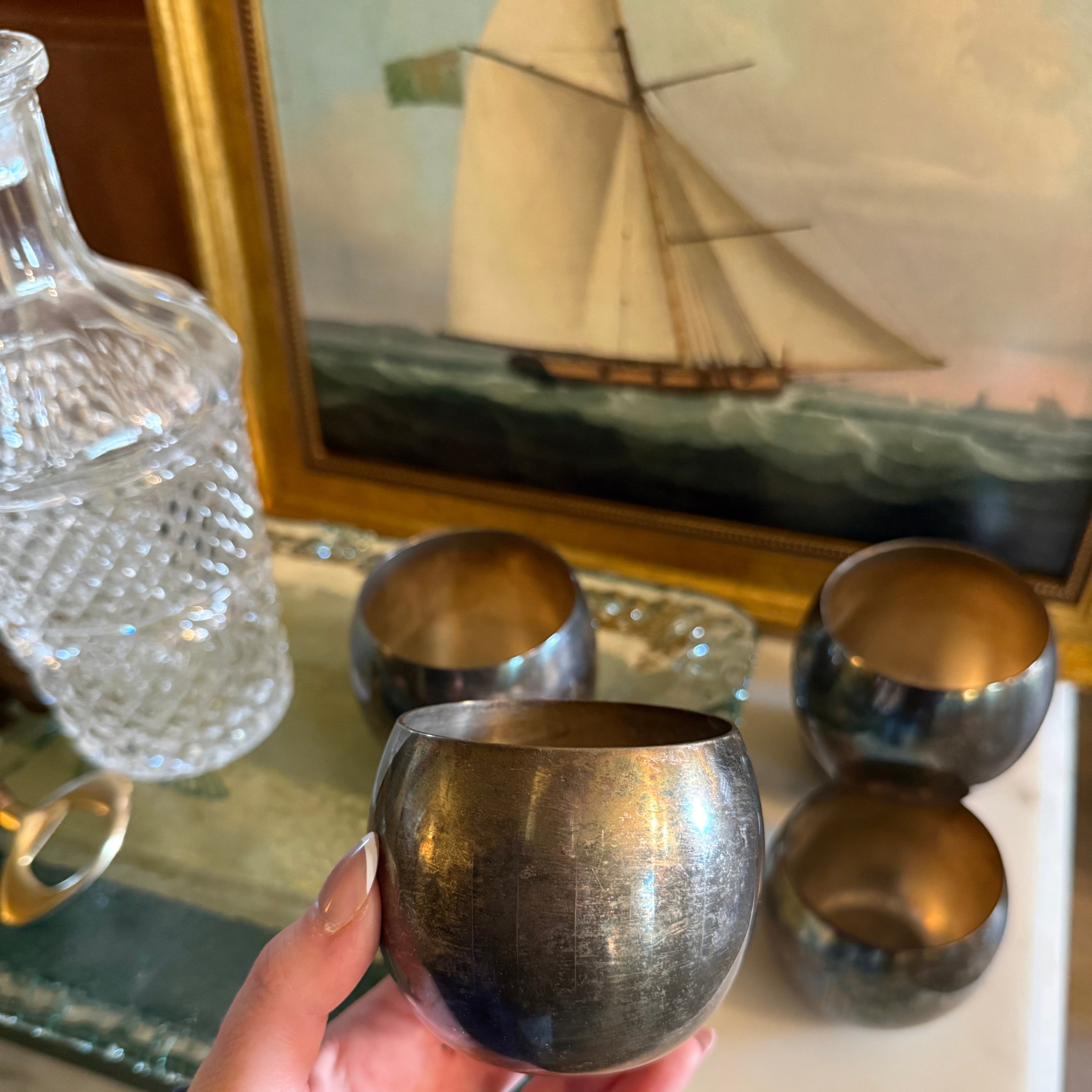 Hand holding a silver goblet in front of a sailboat painting